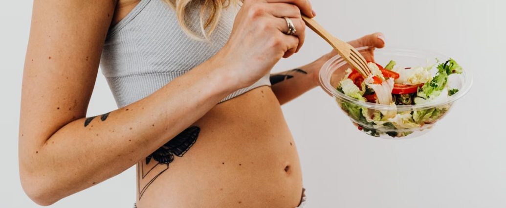 Close-up of a woman in a crop top enjoying a fresh salad indoors.