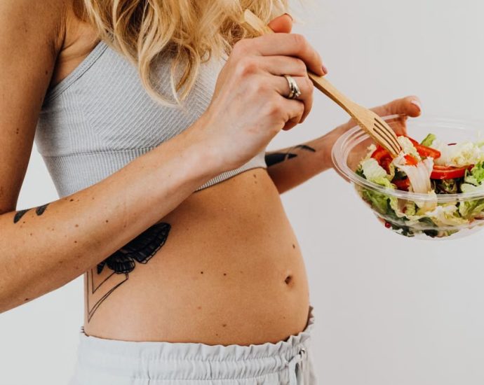 Close-up of a woman in a crop top enjoying a fresh salad indoors.